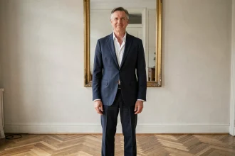 Portrait en pied d'un homme grand et élégant en blazer marine, debout dans un intérieur parisien avec parquet en bois, illustrant la silhouette et la taille de Marc Lavoine